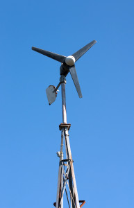 Small domestic wind turbine generator mounted on a vertical frame against a clear blue sky